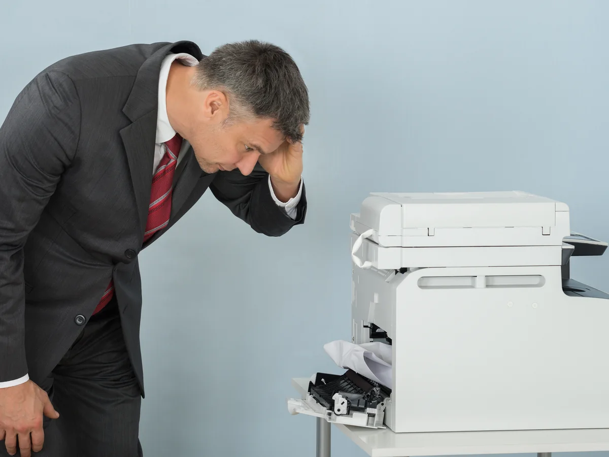 Frustrated businessman troubleshooting a paper jam in an office copier